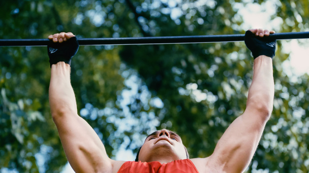 low angle view of strong sportsman doing pull ups on horizontal bar outside - Fotó, kép