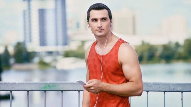 young sportsman holding smartphone and listening music in earphones - Photo, Image