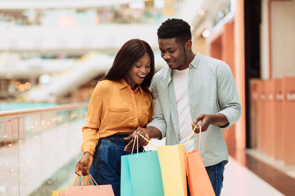 Glückliches schwarzes Paar hält Einkaufstüten in der Hand und schaut hinein - Foto, Bild