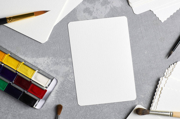 Blank paper card mockup for watercolor drawing, artwork or illustration. White card with paintbrush and watercolor paints palette - Zdjęcie, obraz