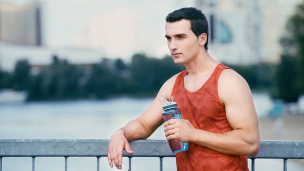 tired sportsman standing on bridge with sports bottle - Foto, Imagen