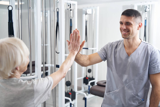 Pleased man medical professional giving high five to senior patient - Zdjęcie, obraz