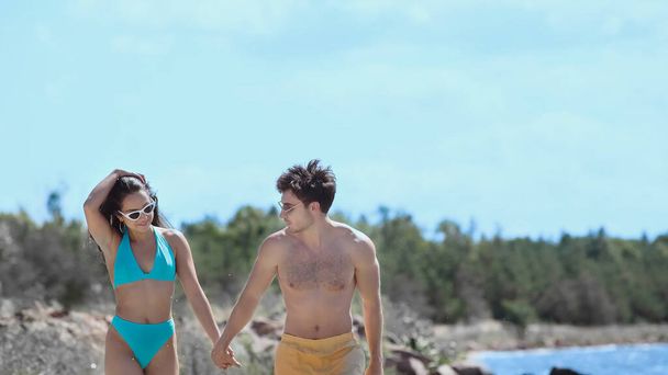 Plajda mayo giymiş gülümseyen bir kadın erkek arkadaşının elini tutuyor.  - Fotoğraf, Görsel