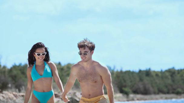 Cheerful couple in swimwear holding hands on beach  - Photo, Image