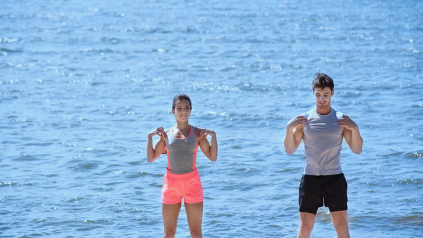 Young brunette couple training near sea on beach  - 写真・画像