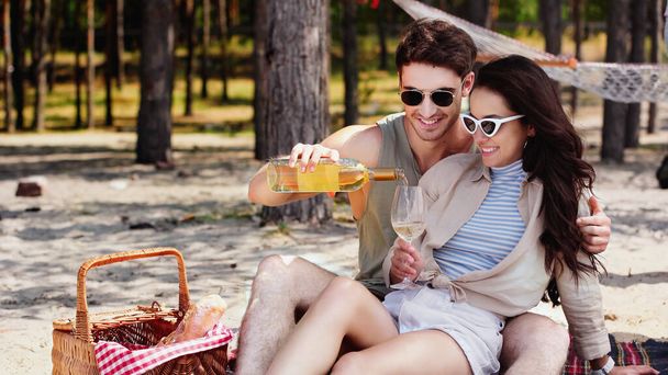 Man in sunglasses pouring wine near girlfriend on beach  - Foto, Imagen