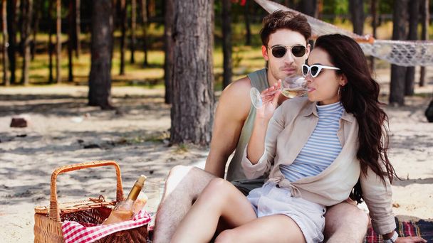 Woman in sunglasses drinking wine near boyfriend on beach  - 写真・画像