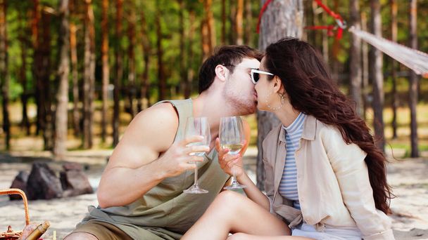 Couple in sunglasses holding wine and kissing on beach  - 写真・画像