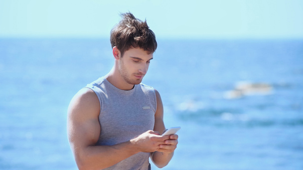 Athletic sportsman using smartphone near blurred sea  - Фото, зображення