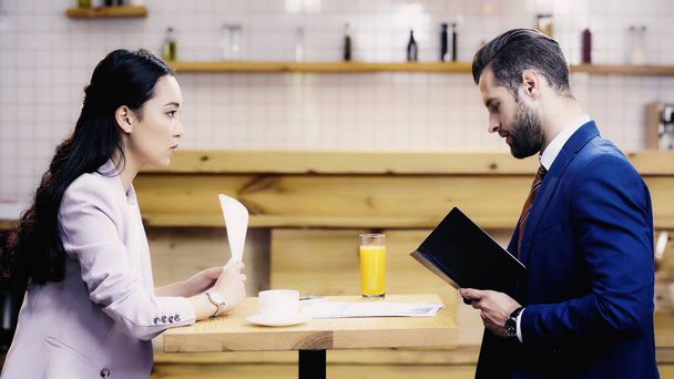 Предпринимательница смотрит сбоку на бородатого бизнесмена в кафе - Фото, изображение