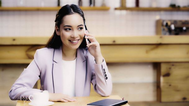 happy asian businesswoman in suit talking on smartphone in cafe  - Fotografie, Obrázek