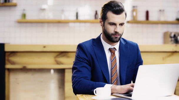 bearded businessman in suit using laptop near cup in cafe - Foto, afbeelding