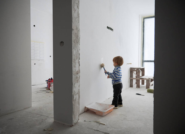 Cute little boy painting wall in apartment under renovation. - Photo, Image