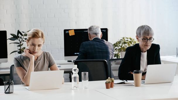 Επιχειρηματίες με επίσημη ένδυση που χρησιμοποιούν φορητούς υπολογιστές κοντά σε συνάδελφο στο γραφείο  - Φωτογραφία, εικόνα