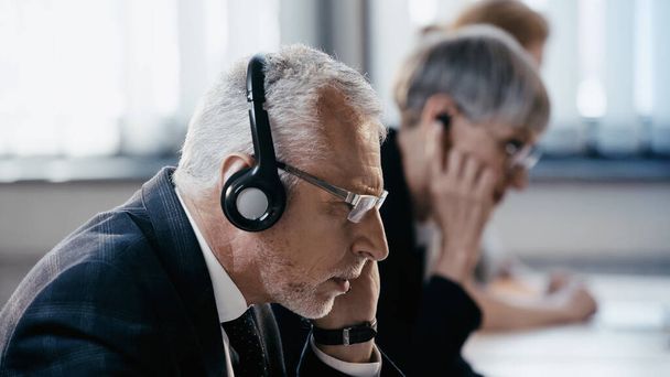 Side view of middle aged businessman in headset working in office  - Фото, изображение