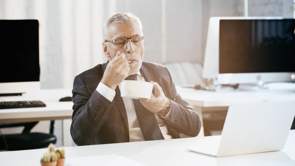 Reifer Geschäftsmann isst Imbisssalat in der Nähe von Laptop im Büro  - Foto, Bild