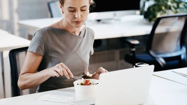 Businesswoman sitting near takeaway salad and laptop in office  - Photo, Image