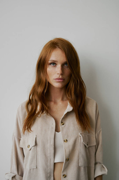 Portrait of young amazing redhead girl in beige shirt on neutral background. Long wavy healthy hair. Beautiful and fresh. Natural beauty. Minimalism. Soft light. Good quality. Hair advertising. Fantastic eyes, big lips. Freckles - 写真・画像