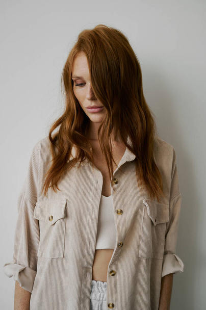 Portrait of young amazing redhead girl in beige shirt on neutral background. Long wavy healthy hair. Beautiful and fresh. Natural beauty. Minimalism. Soft light. Good quality. Hair advertising. Fantastic eyes, big lips. Freckles - Foto, Imagem