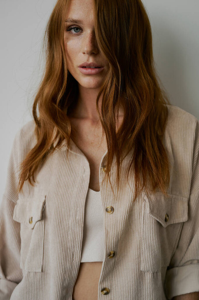 Portrait of young amazing redhead girl in beige shirt on neutral background. Long wavy healthy hair. Beautiful and fresh. Natural beauty. Minimalism. Soft light. Good quality. Hair advertising. Fantastic eyes, big lips. Freckles - Photo, Image
