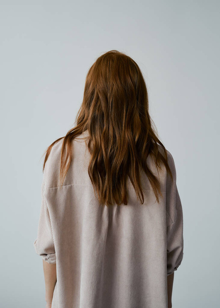 Portrait of young amazing redhead girl in beige shirt on neutral background. Long wavy healthy hair. Beautiful and fresh. Natural beauty. Minimalism. Soft light. Good quality. Hair advertising. No face. - Foto, Bild