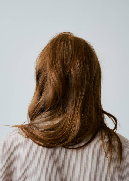Portrait of young amazing redhead girl in beige shirt on neutral background. Long wavy healthy hair. Beautiful and fresh. Natural beauty. Minimalism. Soft light. Good quality. Hair advertising. No face. - Photo, Image