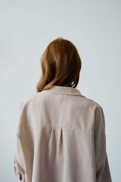 Portrait of young amazing redhead girl in beige shirt on neutral background. Long wavy healthy hair. Beautiful and fresh. Natural beauty. Minimalism. Soft light. Good quality. Hair advertising. No face. - 写真・画像