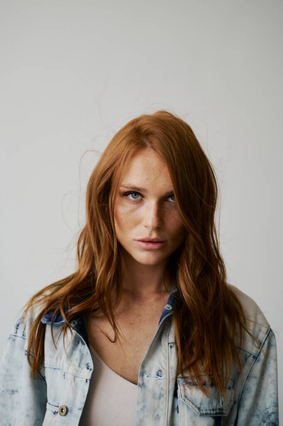 Nice model with red hair, blue eyes and long wavy red hair. Sensual attractive woman. Freckles. Neutral background. Excellent quality. Soft light. Jeans jacket. Nice lashes, big lips, beautiful eyes - Fotografie, Obrázek