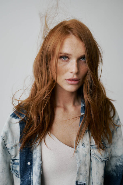 Nice model with red hair, blue eyes and long wavy red hair. Sensual attractive woman. Freckles. Neutral background. Excellent quality. Soft light. Jeans jacket. Nice lashes, big lips, beautiful eyes - Fotoğraf, Görsel