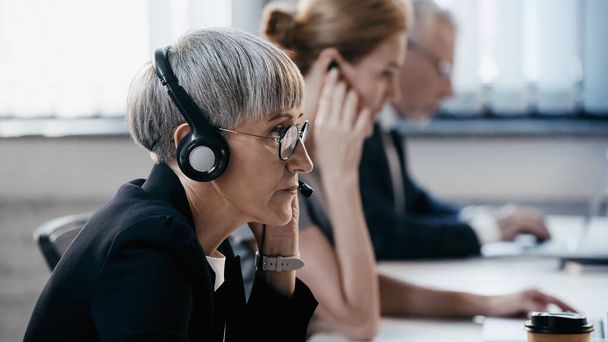 volwassen zakenvrouw in bril en headset werken in kantoor  - Foto, afbeelding