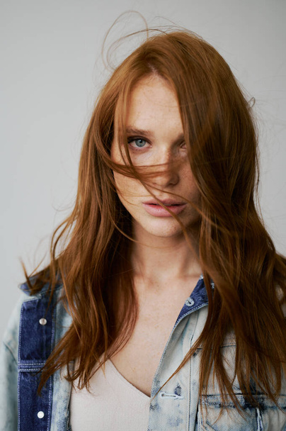Nice model with red hair, blue eyes and long wavy red hair. Sensual attractive woman. Freckles. Neutral background. Excellent quality. Soft light. Jeans jacket. Nice lashes, big lips, beautiful eyes - Фото, изображение