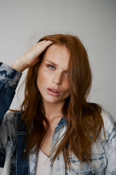 Nice model with red hair, blue eyes and long wavy red hair. Sensual attractive woman. Freckles. Neutral background. Excellent quality. Soft light. Jeans jacket. Nice lashes, big lips, beautiful eyes - Φωτογραφία, εικόνα