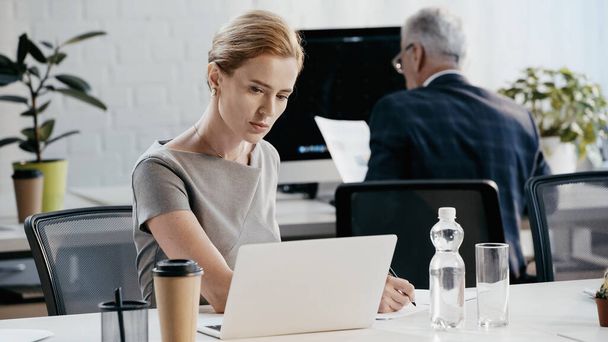 Businesswoman in formal wear writing on paper near laptop in office  - Фото, зображення