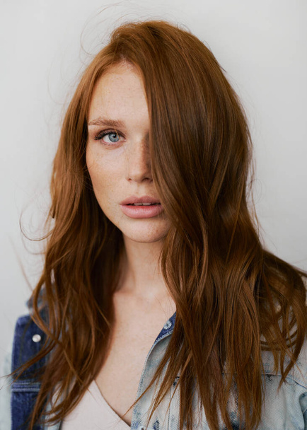 Nice model with red hair, blue eyes and long wavy red hair. Sensual attractive woman. Freckles. Neutral background. Excellent quality. Soft light. Jeans jacket. Nice lashes, big lips, beautiful eyes - Foto, imagen