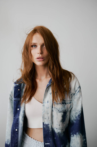 Nice model with red hair, blue eyes and long wavy red hair. Sensual attractive woman. Freckles. Neutral background. Excellent quality. Soft light. Jeans jacket. Nice lashes, big lips, beautiful eyes - Photo, image