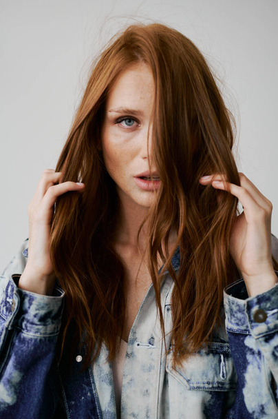 Nice model with red hair, blue eyes and long wavy red hair. Sensual attractive woman. Freckles. Neutral background. Excellent quality. Soft light. Jeans jacket. Nice lashes, big lips, beautiful eyes - 写真・画像