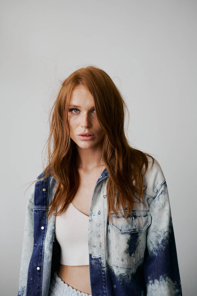 Nice model with red hair, blue eyes and long wavy red hair. Sensual attractive woman. Freckles. Neutral background. Excellent quality. Soft light. Jeans jacket. Nice lashes, big lips, beautiful eyes - Foto, Imagem