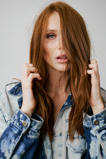 Nice model with red hair, blue eyes and long wavy red hair. Sensual attractive woman. Freckles. Neutral background. Excellent quality. Soft light. Jeans jacket. Nice lashes, big lips, beautiful eyes - Photo, image