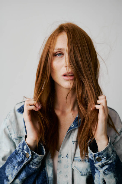 Nice model with red hair, blue eyes and long wavy red hair. Sensual attractive woman. Freckles. Neutral background. Excellent quality. Soft light. Jeans jacket. Nice lashes, big lips, beautiful eyes - Foto, imagen