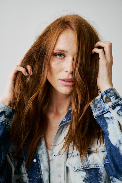 Nice model with red hair, blue eyes and long wavy red hair. Sensual attractive woman. Freckles. Neutral background. Excellent quality. Soft light. Jeans jacket. Nice lashes, big lips, beautiful eyes - Photo, Image