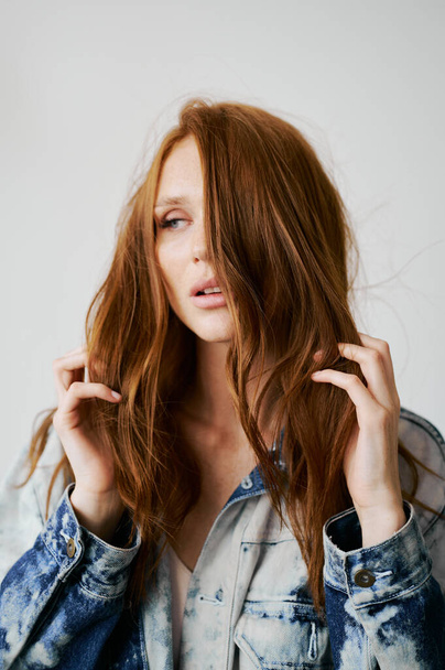 Nice model with red hair, blue eyes and long wavy red hair. Sensual attractive woman. Freckles. Neutral background. Excellent quality. Soft light. Jeans jacket. Nice lashes, big lips, beautiful eyes - Zdjęcie, obraz