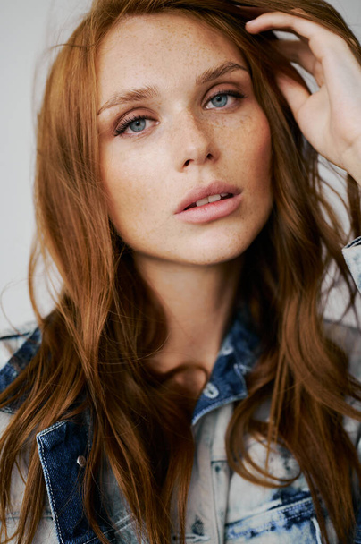 Nice model with red hair, blue eyes and long wavy red hair. Sensual attractive woman. Freckles. Neutral background. Excellent quality. Soft light. Jeans jacket. Nice lashes, big lips, beautiful eyes - Foto, Bild