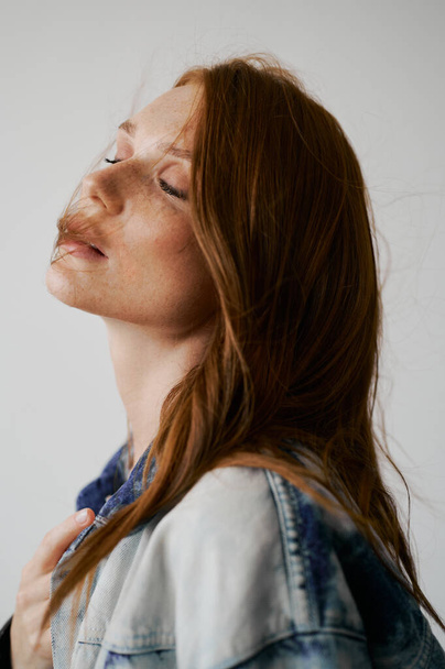 Nice model with red hair, blue eyes and long wavy red hair. Sensual attractive woman. Freckles. Neutral background. Excellent quality. Soft light. Jean jacket. Nice lashes, big lips, beautiful eyes - Fotografie, Obrázek