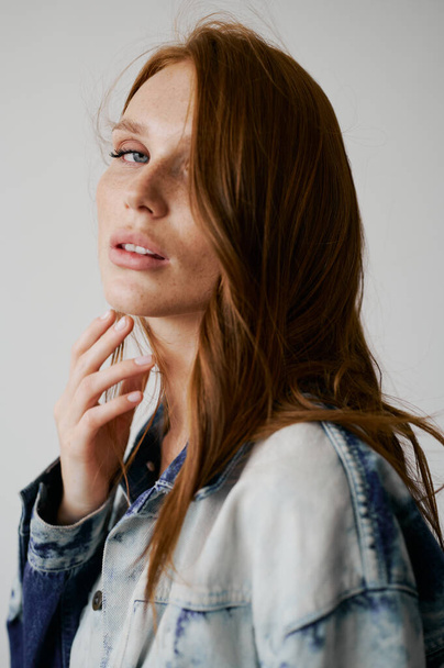 Nice model with red hair, blue eyes and long wavy red hair. Sensual attractive woman. Freckles. Neutral background. Excellent quality. Soft light. Jean jacket. Nice lashes, big lips, beautiful eyes - Foto, imagen