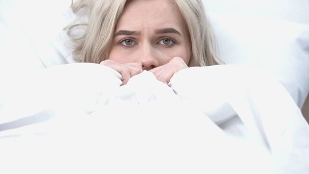 молодая расстроенная женщина смотрит в камеру в постели - Фото, изображение