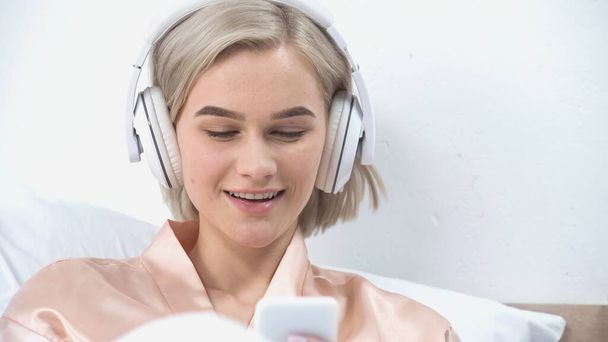 Kablosuz kulaklıklı neşeli genç kadın müzik dinliyor ve akıllı telefon kullanıyor.  - Fotoğraf, Görsel