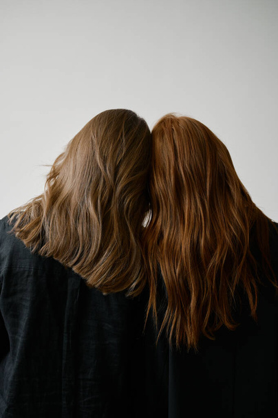 Hair advertising. Two redhead girls in black clothes on neutral background. Good long wavy hair. Pretty tall models. Natural beauty. Minimalism. Stylish, fashionable. Soft light. Care and repair. No faces - Foto, imagen