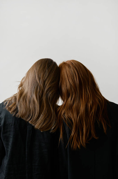 Hair advertising. Two redhead girls in black clothes on neutral background. Good long wavy hair. Pretty tall models. Natural beauty. Minimalism. Stylish, fashionable. Soft light. Care and repair. No faces - Foto, Imagem