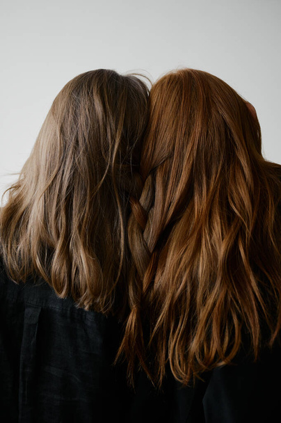 Hair advertising. Two redhead girls in black clothes on neutral background. Good long wavy hair. Pretty tall models. Natural beauty. Minimalism. Stylish, fashionable. Soft light. Care and repair. No faces - Photo, Image