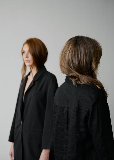 Hair advertising. Two redhead girls in black clothes on neutral background. Good long wavy hair. Pretty tall models. Natural beauty. Minimalism. Stylish, fashionable. Soft light. Care and repair. Back and front views - Fotó, kép